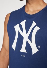 Laivastonsininen hihaton toppi, joka on valmistettu puuvillasta ja jossa on iso valkoinen New York Yankees -logo edessä. Siistit linjat, pyöreä pääntie.
