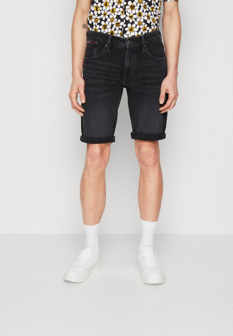 Pantalones cortos de mezclilla negra con dobladillos enrollados, que cuentan con bolsillos frontales y un cierre de botón, llevados con calcetines blancos y zapatillas. Camisa de patrón floral.