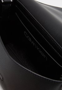 Detailní záběr na černou koženou tašku Calvin Klein uvnitř, s viditelným logem značky na vnitřním podšívce.