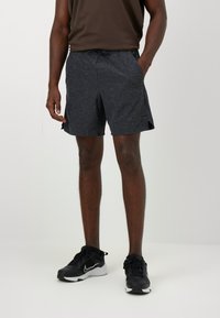 Calções desportivos pretos com um tecido texturizado, cintura elástica, bolsos laterais e fendas na bainha, combinados com sapatilhas pretas.