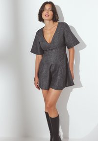 Siva teksturirana obleka z globokim V-izrezom, kratkimi širokimi rokavi in A-linijo, v par z črnimi škornji do kolen.