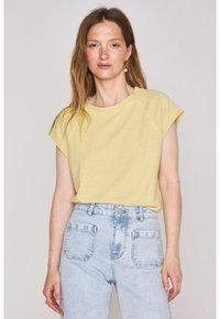 T-shirt giallo chiaro a maniche corte con scollo rotondo, abbinato a jeans in denim blu chiaro a vita alta con ampie tasche posteriori.