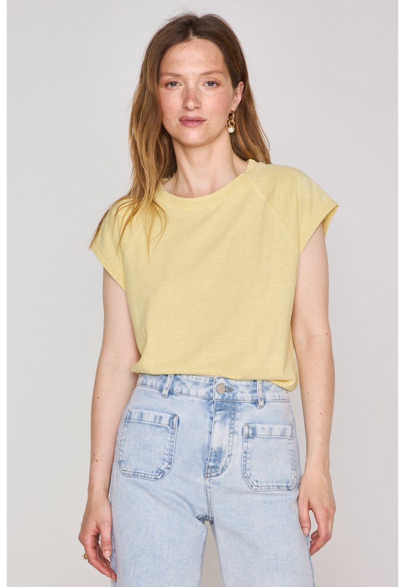 T-shirt giallo chiaro a maniche corte con scollo rotondo, abbinato a jeans in denim blu chiaro a vita alta con ampie tasche posteriori.