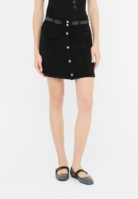 Must have a front button closure and two pockets. The decorative waistband features the brand name. The fabric is soft to the touch.