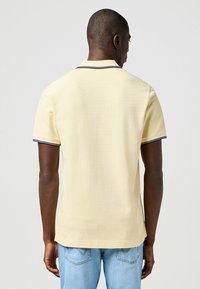 Polohemd aus weichem, gelbem Baumwollstoff mit einem klassischen Kragen, kurzen Ärmeln und dunkelblauen Akzenten am Kragen und an den Manschetten. Einfaches Design, entspannter Schnitt.