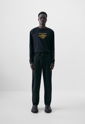 Black long-sleeve shirt with gold text and graphic details, paired with black pants and black shoes. Simple, minimalist design.