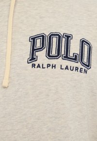 Šedá mikina vyrobená z měkkého materiálu, s modrou vyšitou logem "POLO" a "RALPH LAUREN" pod ním. Obsahuje krémovou šňůrku na stažení.