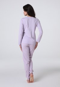 Maglia a manica lunga viola abbinata a pantaloni grigi chiari con un motivo a pois rosa, realizzati in un tessuto morbido e elasticizzato.