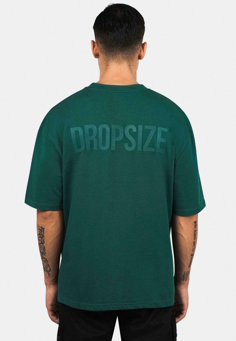 Grünes Baumwoll-T-Shirt mit kurzen Ärmeln, Rundhalsausschnitt und dem Wort "DROPSIZE", das groß und farblich passend auf dem Rücken aufgedruckt ist.