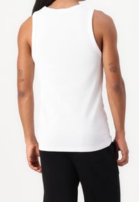White ribbed tank top with a round neckline and sleeveless design. Displaying a smooth texture and a fitted shape.