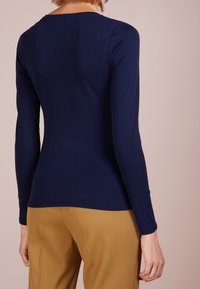 Marinblå långärmad topp med en figurnära design, rund halsringning och mjukt material, tillsammans med ljusbruna byxor. En enkel och ren silhuett.