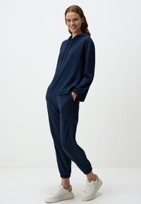 Ensemble de sweat à capuche bleu marine et de jogging assorti en tissu doux ; il présente une coupe décontractée, des poignets élastiques et des poches latérales. Baskets avec accents en daim.
