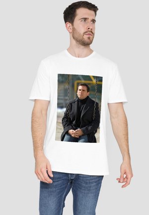 White T-shirt featuring a printed image of a man seated on a swing, wearing a black coat and turtleneck, with a neutral expression.