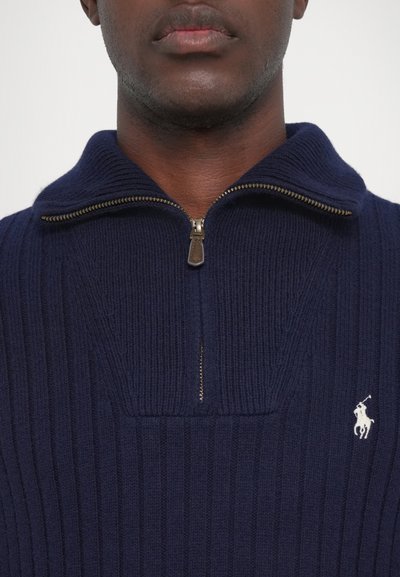 Sudadera de cremallera en color navy con textura acanalada, con un cuello alto y una cremallera dorada. Un pequeño logo blanco es visible en el pecho.
