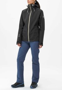 Black waterproof jacket with hood, beige zipper, and gray accents, paired with blue waterproof pants and black hiking shoes with blue details.