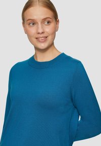 Blauwe trui van zacht materiaal, met een ronde hals, lange mouwen en een gladde textuur met subtiele details langs de naden.