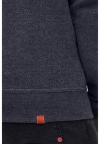 Sudadera gris oscuro con dobladillo acanalado, que presenta un pequeño parche de logo marrón en el borde inferior. Textura suave, diseño deportivo y ajuste casual.