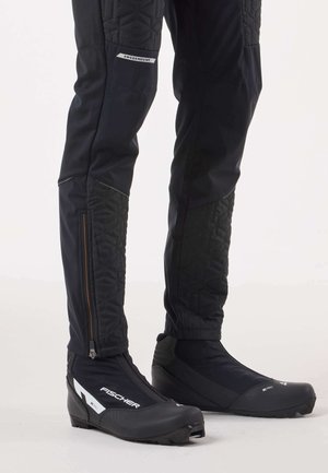 Schwarze Winterhose mit gepolsterten, gesteppte Akzenten und Reißverschlusstaschen, kombiniert mit schwarzen Fischer-Stiefeln mit Reißverschluss und strukturierter Sohle.