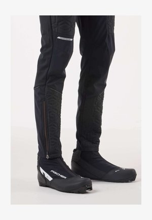 Schwarze Winterhose mit gepolsterten, gesteppte Akzenten und Reißverschlusstaschen, kombiniert mit schwarzen Fischer-Stiefeln mit Reißverschluss und strukturierter Sohle.