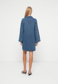 Džinsu kleita ar garām piedurknēm, apkakli un nedaudz platu formu. Iezīmē neapstrādāts apakšmalas un kontrastējoši šuvumi. Krāsa: vidēji zila.