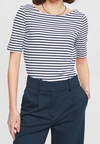 Top de manga corta a rayas en blanco y azul marino, con un escote barco. Combinado con pantalones oscuros, que presentan una textura suave y un ajuste a medida.