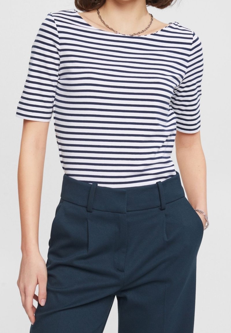 Top de manga corta a rayas en blanco y azul marino, con un escote barco. Combinado con pantalones oscuros, que presentan una textura suave y un ajuste a medida.