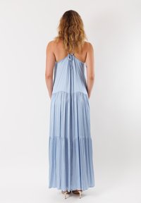 Abito maxi azzurro chiaro con dettagli arricciati sul retro, spalline sottili e gonna a strati. Realizzato in tessuto morbido e fluido.