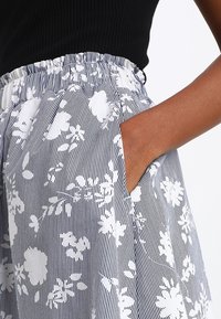 Bloemmotief rok in blauw en wit, met verticale strepen. Elastische tailleband en zij zakken, afgewerkt met fijne stof textuur.