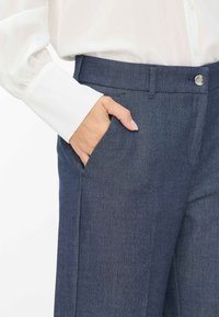Donkerblauwe broek van gestructureerde stof met een voorkeurs zak, voorzien van een gladde tailleband en een metalen knoopsluiting.
