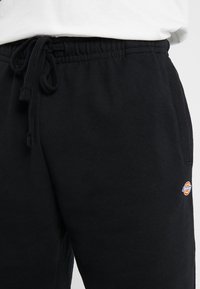 Černé tepláky s elastickým pasem, se stahovací šňůrkou a malou barevnou nášivkou na boku. Měkký materiál, volný střih.