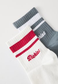 Dva páry ponožiek do členkov: jedny biele s červenými a bielymi pruhmi a vyšitým nápisom "Dickies", druhé šedé s tmavosivým pruhom.