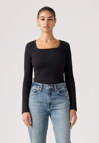 Μαύρο ριμπ τοπ με μακριά μανίκια και τετράγωνη λαιμόκοψη, συνδυασμένο με τζιν παντελόνι σε ευθεία γραμμή και ανοιχτό πλύσιμο. Λείο υλικό, εφαρμοστό σχέδιο.