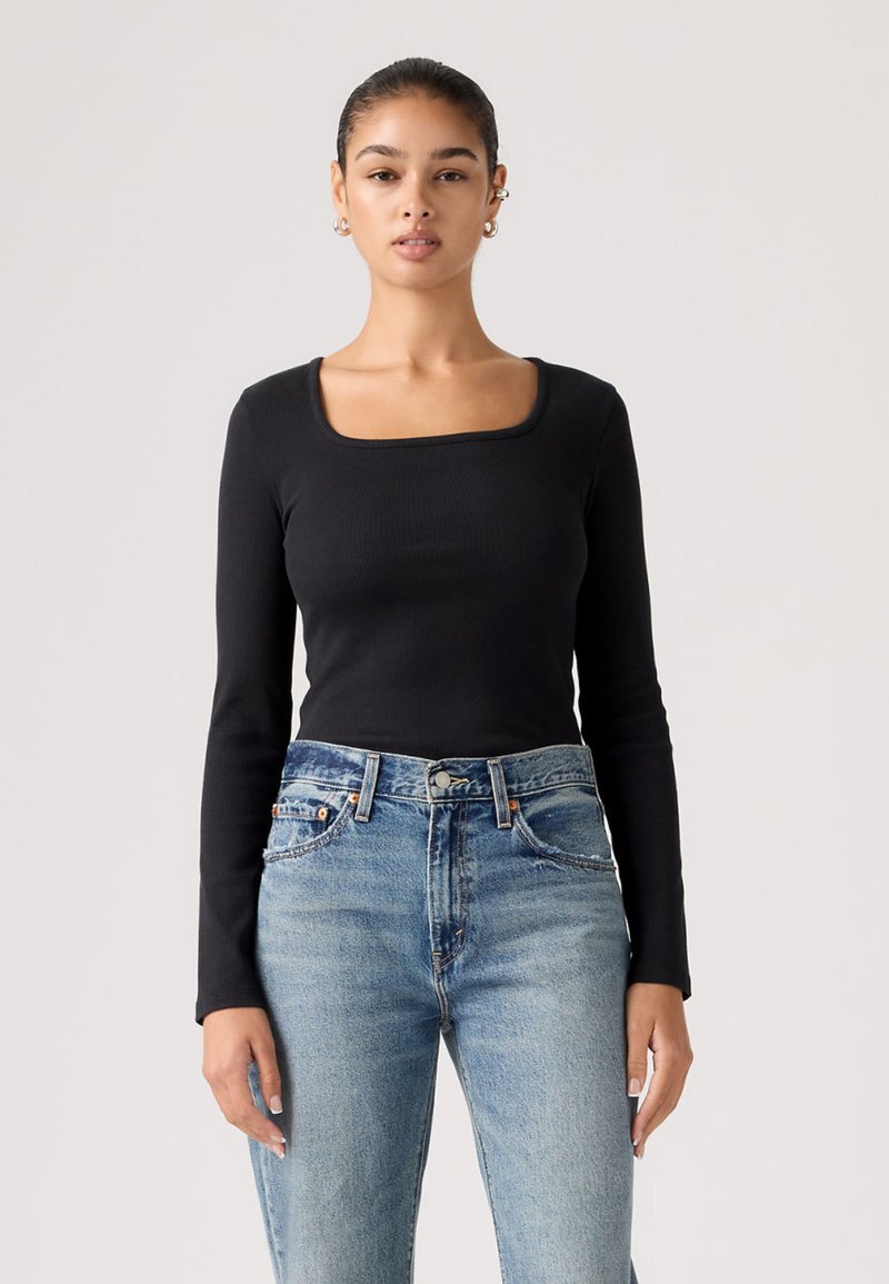 Μαύρο ριμπ τοπ με μακριά μανίκια και τετράγωνη λαιμόκοψη, συνδυασμένο με τζιν παντελόνι σε ευθεία γραμμή και ανοιχτό πλύσιμο. Λείο υλικό, εφαρμοστό σχέδιο.