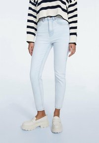 Světlomodré skinny džíny s vysokým pasem, které mají jemně vybledlý vzhled. Kombinované s krémovými masivními mokasíny a proužkovaným svetrem.