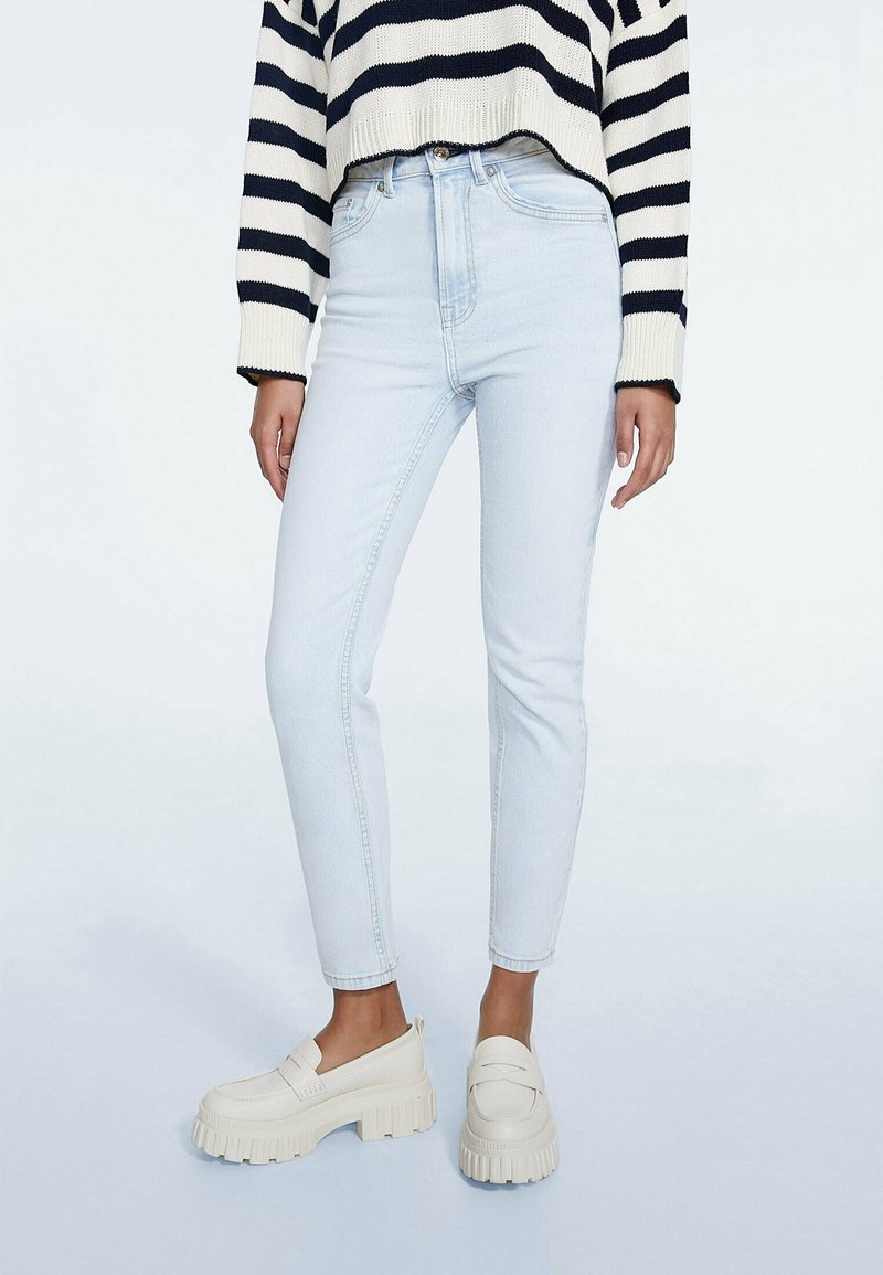 Světlomodré skinny džíny s vysokým pasem, které mají jemně vybledlý vzhled. Kombinované s krémovými masivními mokasíny a proužkovaným svetrem.