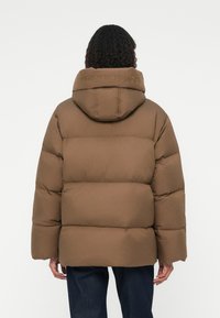 Brun pufferjakke med hætte, udstyret med et quiltet design og præget tekst "TOMMY HILFIGER" på kraven. Blød tekstur og afslappet pasform.