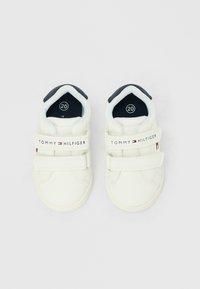 Ζευγάρι λευκά αθλητικά παπούτσια για νήπια με εσωτερική επένδυση σε ναυτικό μπλε, διπλό λουράκι με βέλκρο και επωνυμία "Tommy Hilfiger" στα πάνω λουράκια.