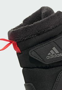 Zwarte sportieve boot met een textiele bovenkant, een zachte binnenvoering en een rode lus. Kenmerkt zich door een opvallend grijs logo aan de zijkant.