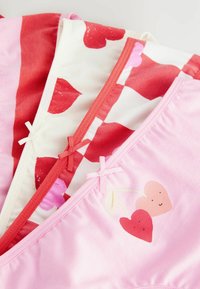 Drei Paare Mädchenunterhosen in Pink, Weiß und Rot. Jede hat verschiedene Herzmuster und leichte Schleifen an den Taillenbündchen.