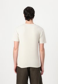 Light beige short-sleeve t-shirt with a ribbed texture, round neckline, and straight hem, worn with dark olive cargo shorts.