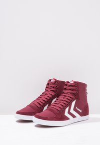 Adidași înalți din pânză burgundă cu accente albe, având un finisaj texturat, șireturi proeminente și un logo pe lateral.