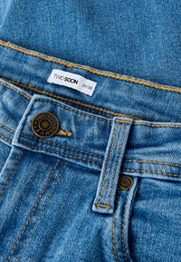 Šviesiai mėlynos spalvos džinsai su sagomis, ryškiai rudos siūlės, ir prekės ženklo etiketė su užrašu „TWO SOON“, dydis 31/32.