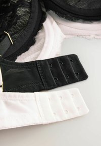 Sostenitori neri e bianchi esposti, con dettagli in pizzo, spalline regolabili e chiusure a gancio e occhiello. Il reggiseno nero ha una fascia testurizzata.