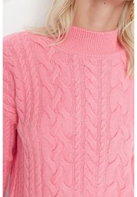 Pull en maille torsadée rose avec un col montant, une texture douce et des motifs en tresses bien marqués.