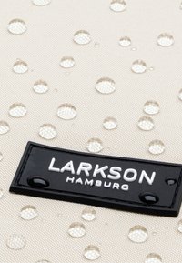 Tessuto resistente all'acqua in beige con gocce chiare in rilievo, caratterizzato da un'etichetta rettangolare nera impresso con il testo "LARKSON HAMBURG."