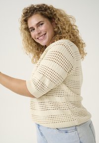 Pull en tricot de couleur crème clair avec un design à mailles ouvertes texturé, présentant des manches courtes et une coupe décontractée.