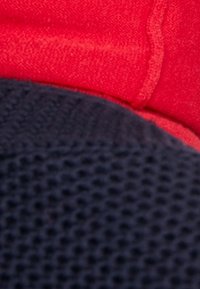 Tessuto blu navy con un motivo a rete incontra un tessuto rosso liscio. I materiali sono sovrapposti, mettendo in risalto il contrasto di colore e texture.