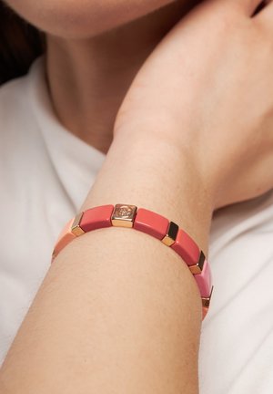 Bunter Armband mit ineinandergreifenden Segmenten in Rosa- und Koralltönen, mit goldenen Akzenten und einem zentralen dekorativen Detail. Glatte Textur.
