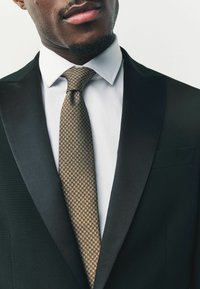 Mustat frakki takki satiinikauluksilla, valkoinen paita ja tummanruskea solmio, jossa on houndstooth-kuvio.