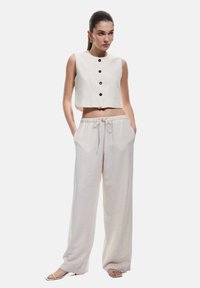 Top corto in lino chiaro con bottoni neri abbinato a pantaloni larghi con cordoncino. Tessuto morbido, vestibilità rilassata, design minimalista.